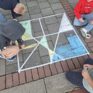 Kinder malen mit Kreide geometrische Figuren auf den Schulhof.