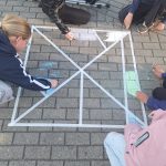 Kinder malen mit Kreide geometrische Figuren auf den Schulhof. 